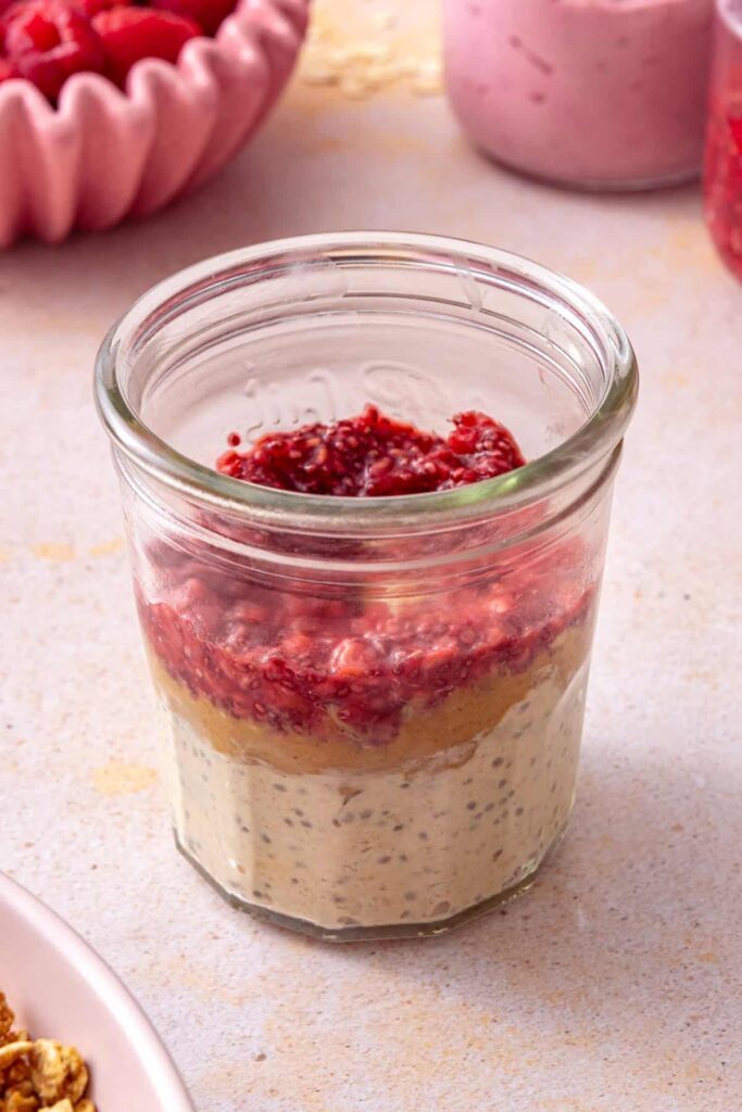 Layering peanut butter overnight oats with raspberry chia jam in glass jars