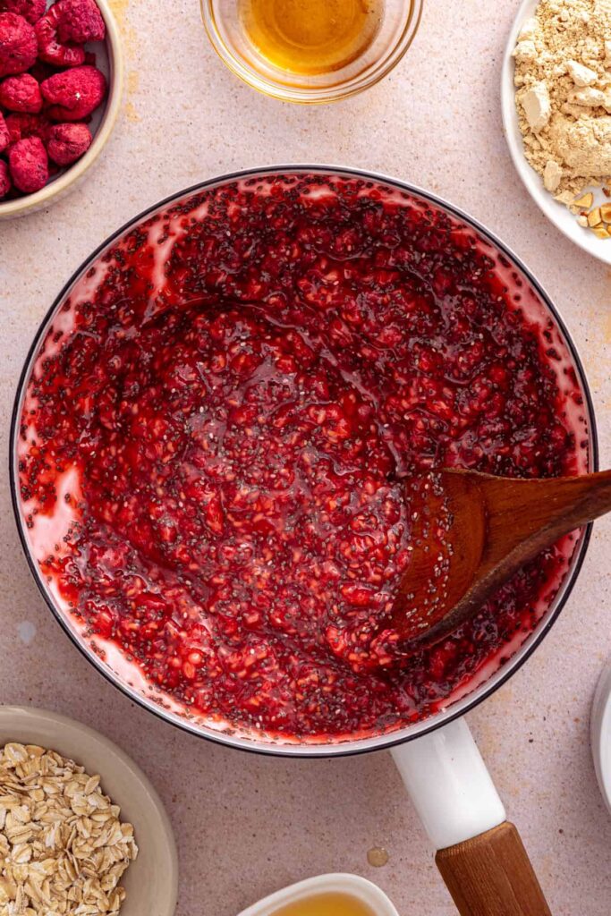 stirring a chia seed-thickened raspberry jam for a gluten-free overnight oats recipe