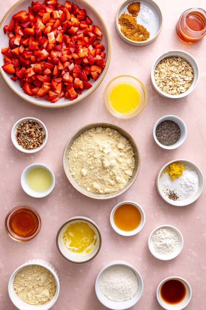 Ingredients to make homemade strawberry oatmeal bars including strawberries, almond flour, oats, maple syrup, chia seeds, and butter.