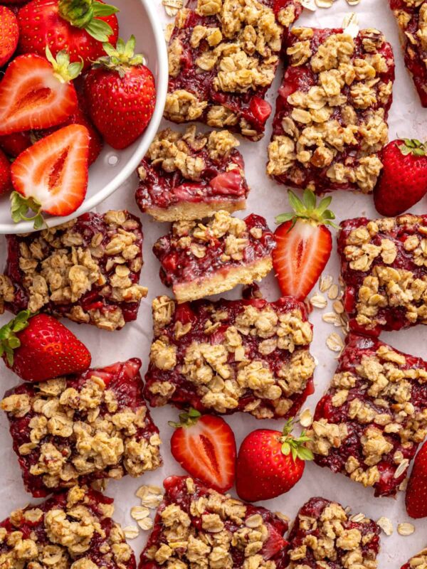 Homemade strawberry oatmeal bars with a buttery oat crumble topping arranged on a table with fresh sliced strawberries.