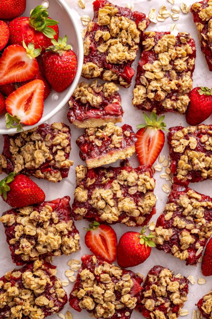 Homemade strawberry oatmeal bars with a buttery oat crumble topping arranged on a table with fresh sliced strawberries.