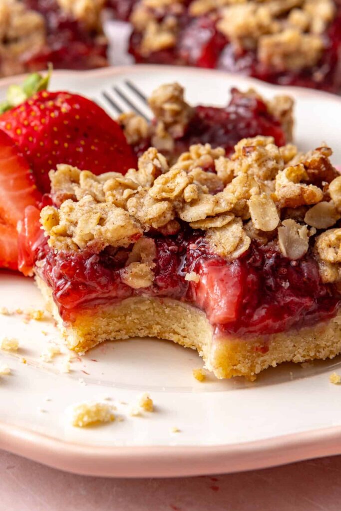 Close-up of a strawberry crumble bar with a fork and fresh strawberries.
