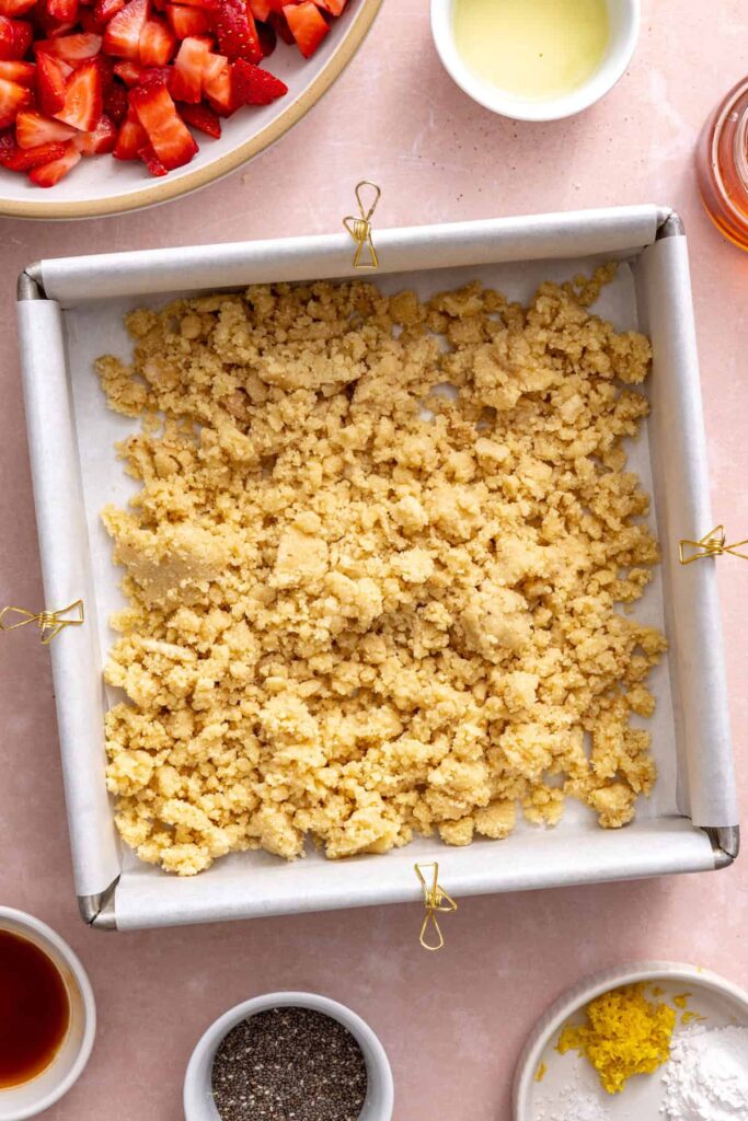 Pressing the gluten-free crust into a parchment-lined baking pan for strawberry oatmeal bars.