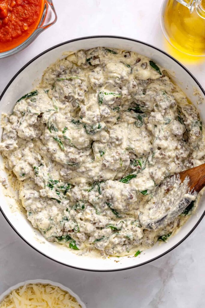 Mixing pesto beef filling into whipped ricotta for stuffed shells assembly
