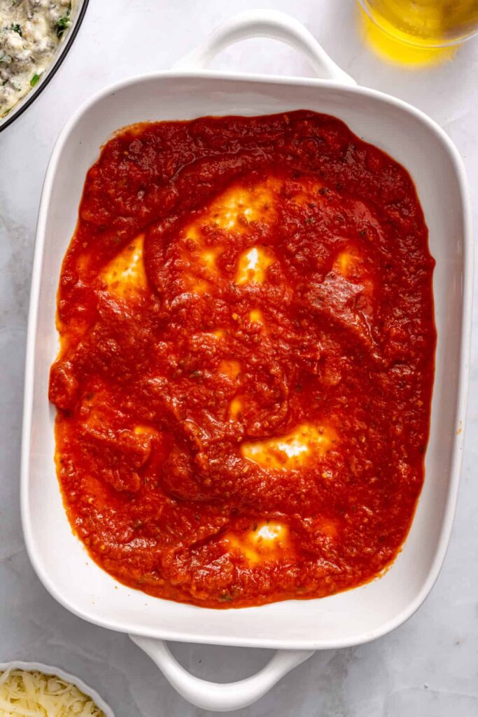Marinara sauce spread evenly in bottom of baking dish for stuffed shells base layer