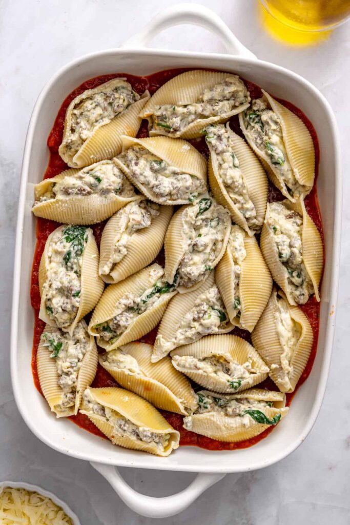 Filled pasta shells being arranged in baking dish for baked stuffed shells preparation
