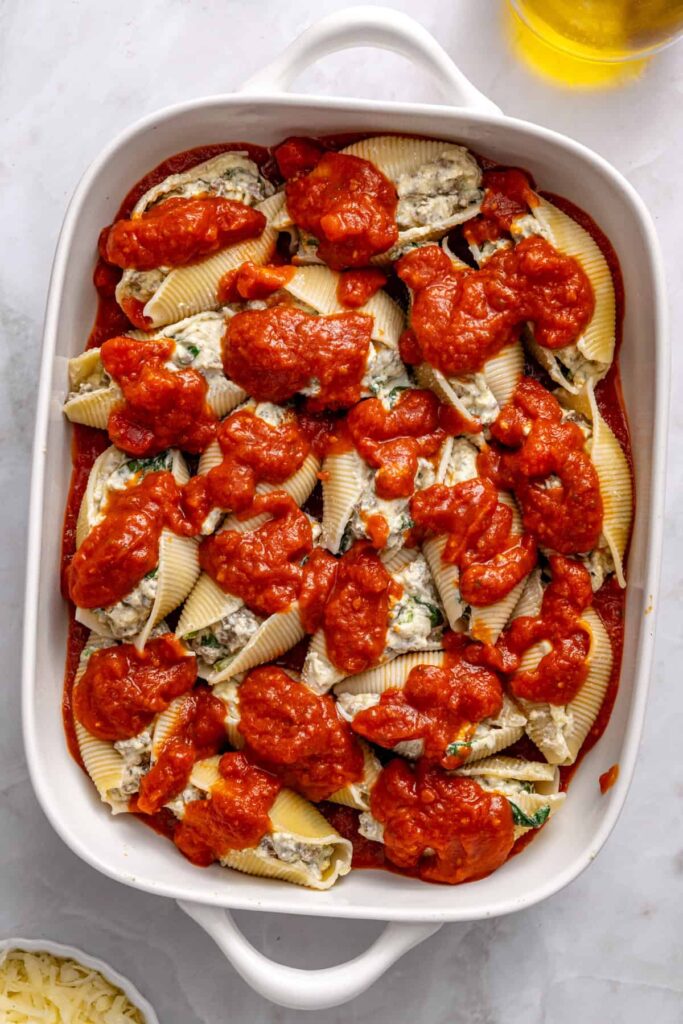 Stuffed shells topped with marinara sauce before baking