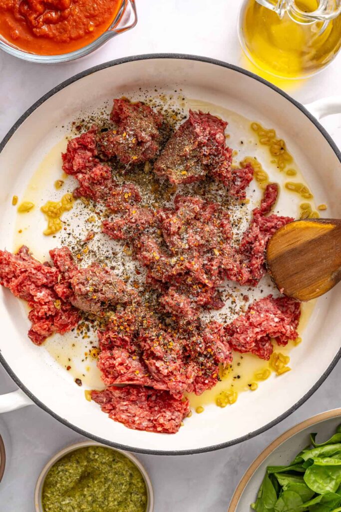 Ground beef browning in skillet with garlic and seasoning for stuffed shells filling