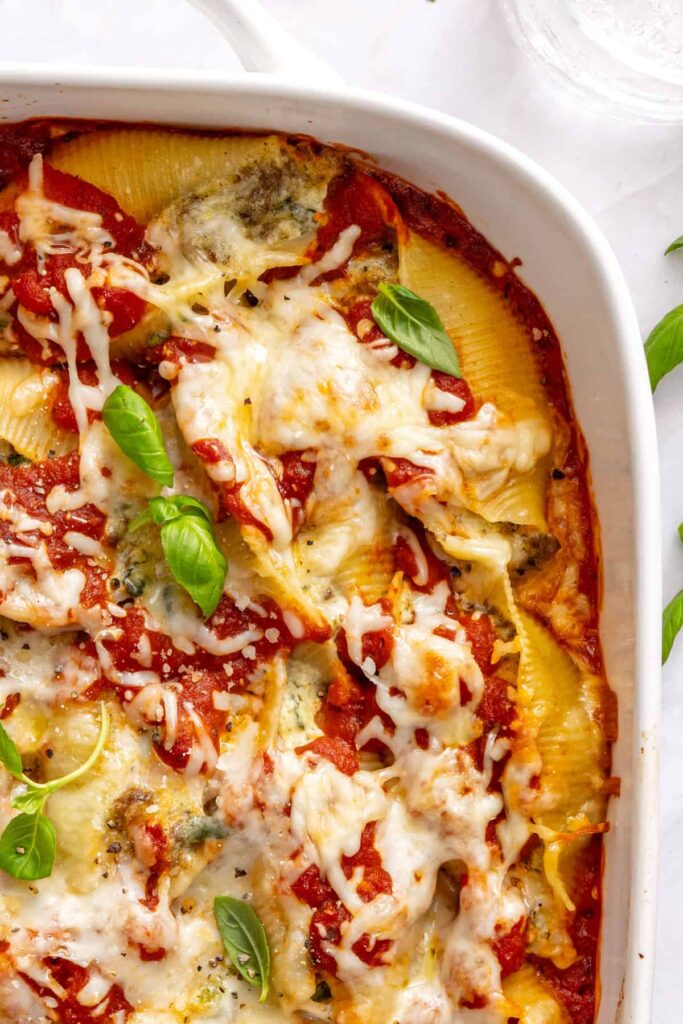 Styled overhead shot of stuffed shells in baking dish with herbs and olive oil on side of table