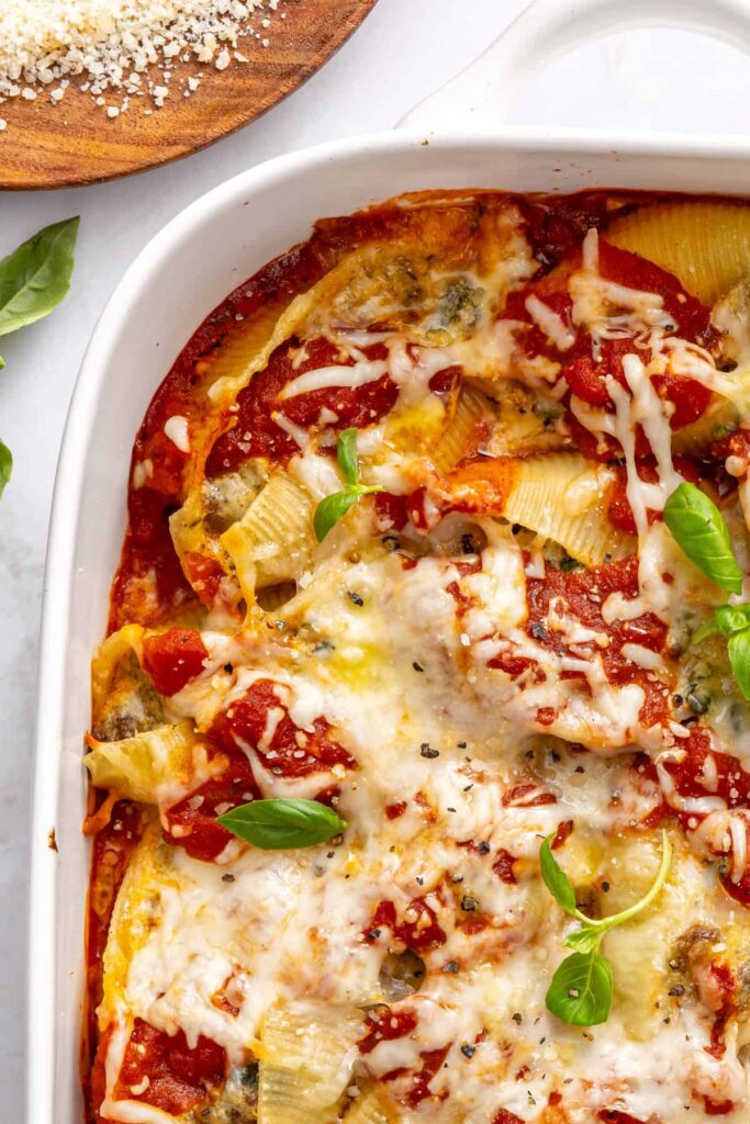 Overhead angled shot of stuffed shells in baking dish placed on a styled table with fresh basil and serving accessories