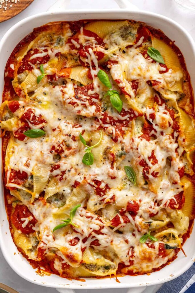 Top-down view of cheesy stuffed shells baked in marinara sauce with basil garnish in a 9x13 dish on a table setting