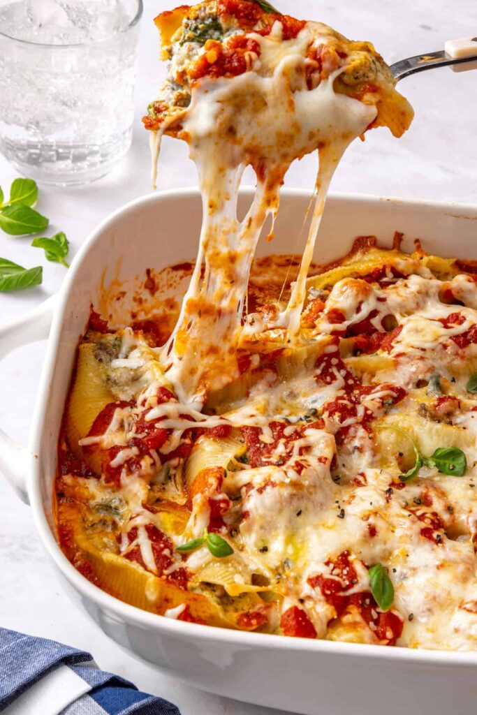 Close-up action shot of stuffed shells being served with visible cheese pull and creamy ricotta filling