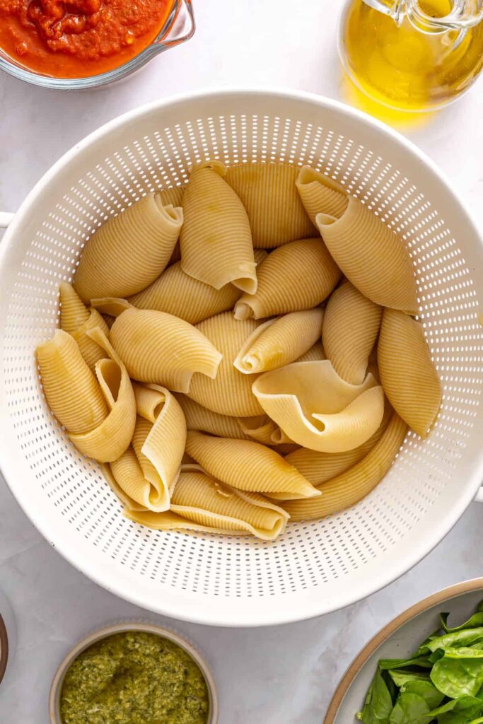 Cooked pasta shells set aside in colander for pesto beef stuffed shells filling process