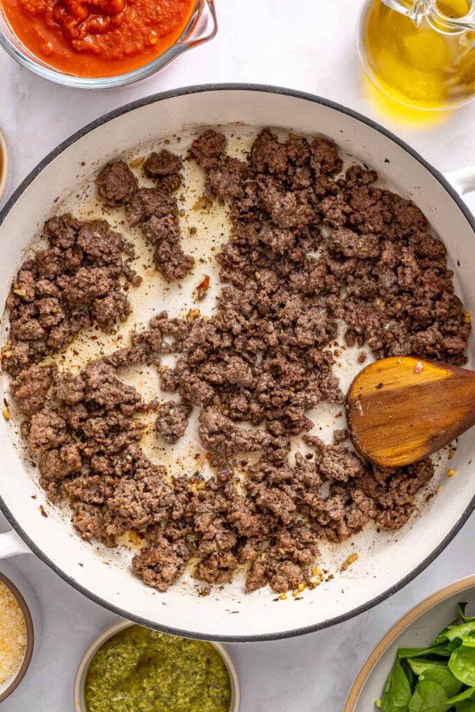 Cooking seasoned ground beef in pan for pesto beef and spinach stuffed shells mixture