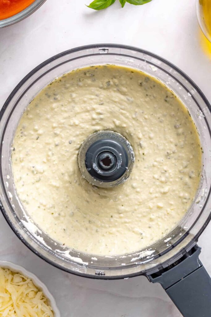 Smooth whipped ricotta filling for stuffed shells being prepared in blender with pesto and cheese