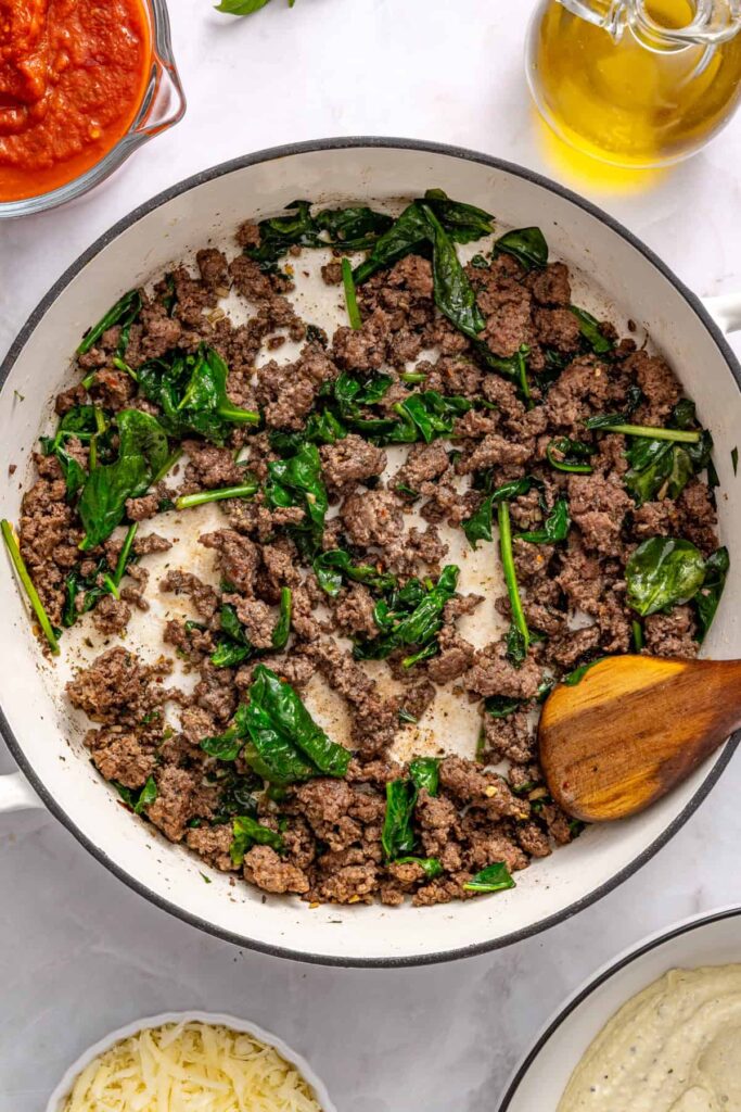 Spinach cooking down in skillet with seasoned beef for pesto stuffed shells recipe