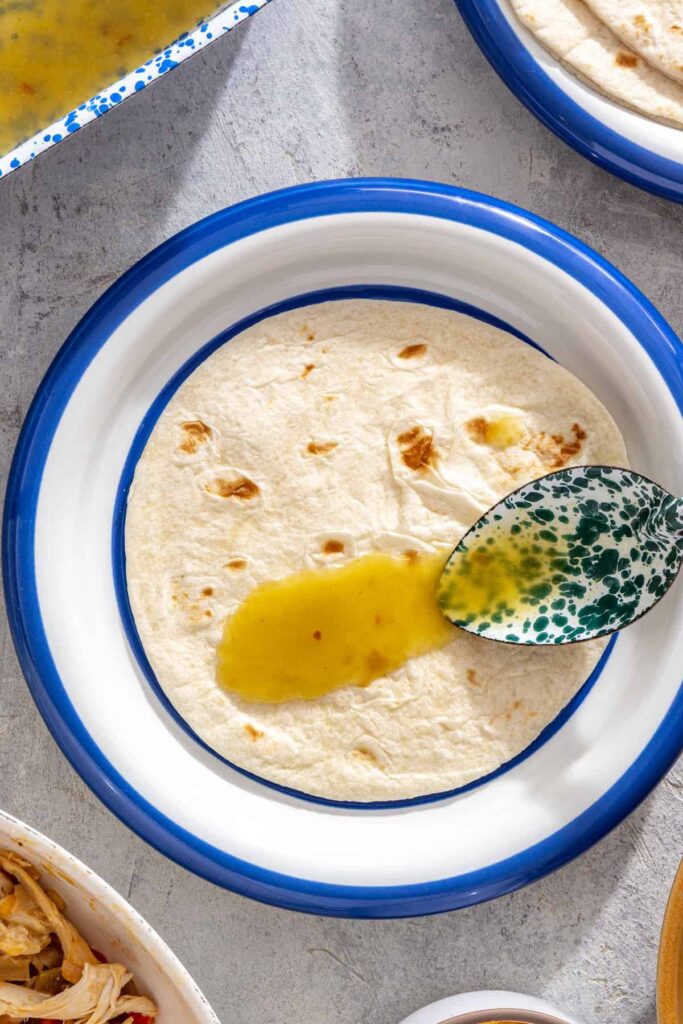 spooning enchilada sauce on warmed tortilla for creamy green chicken enchiladas