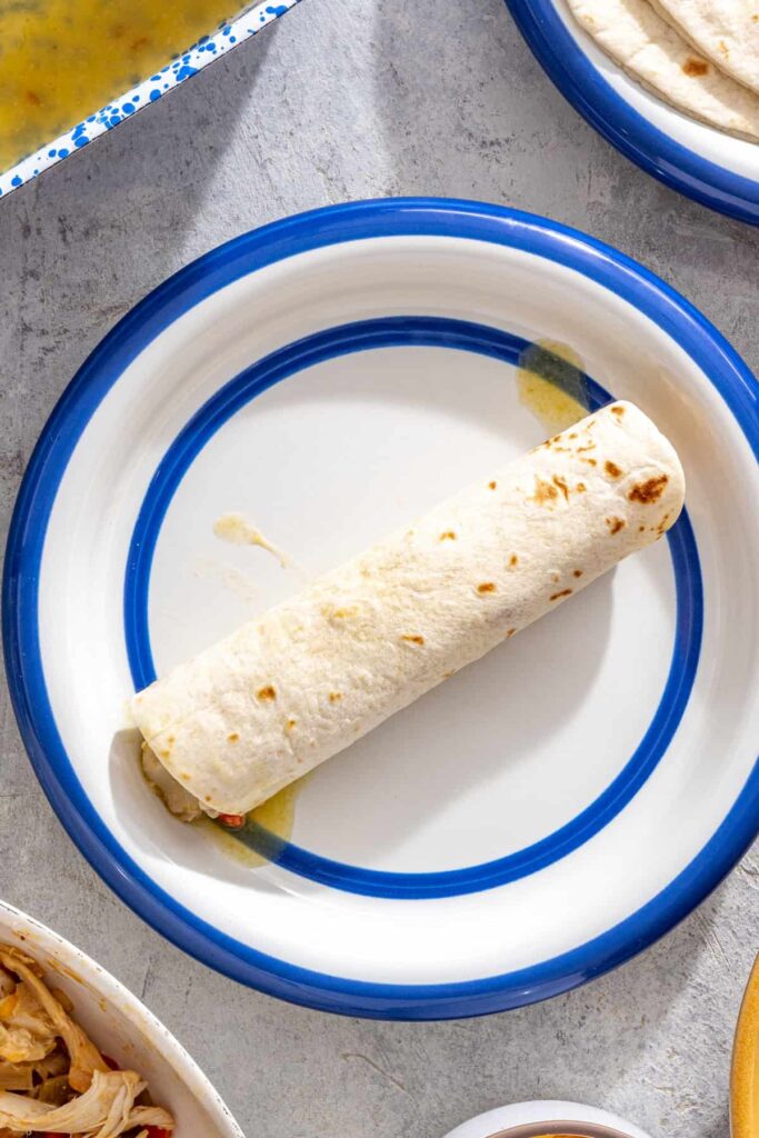Rolling creamy green chicken enchiladas before baking