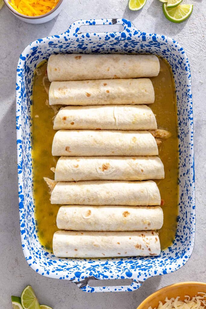 Rolled chicken enchiladas arranged seam-side down in a baking dish