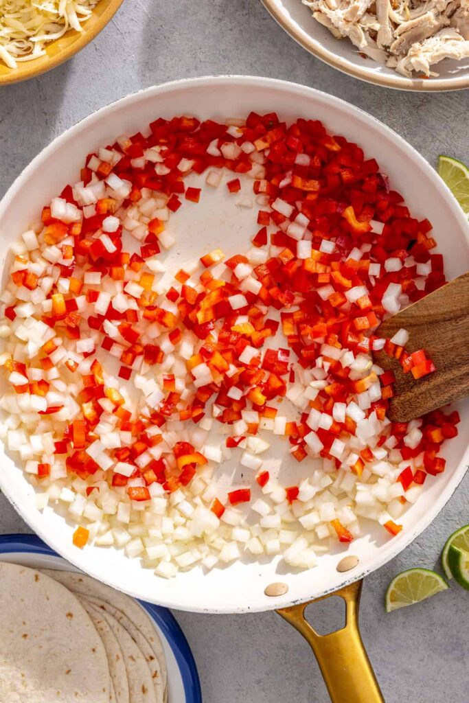 Diced onion and bell pepper cooking in a skillet for creamy green chicken enchiladas