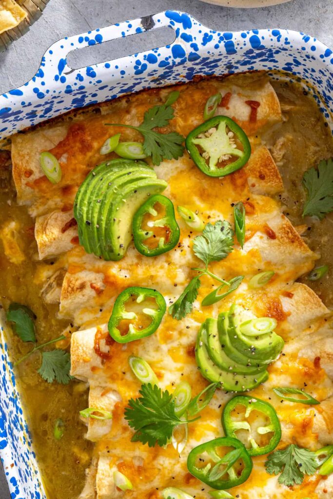 close-up of garnished creamy green chicken enchiladas in a speckled baking dish