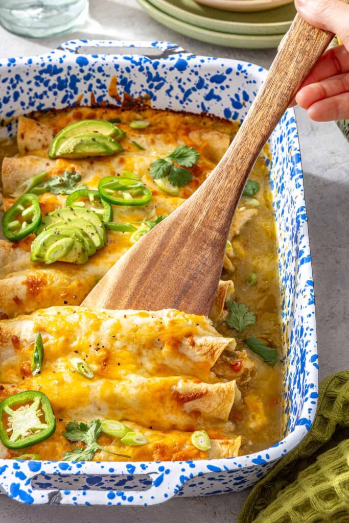 Wooden spatula lifting a creamy chicken enchilada with melted cheese and salsa verde