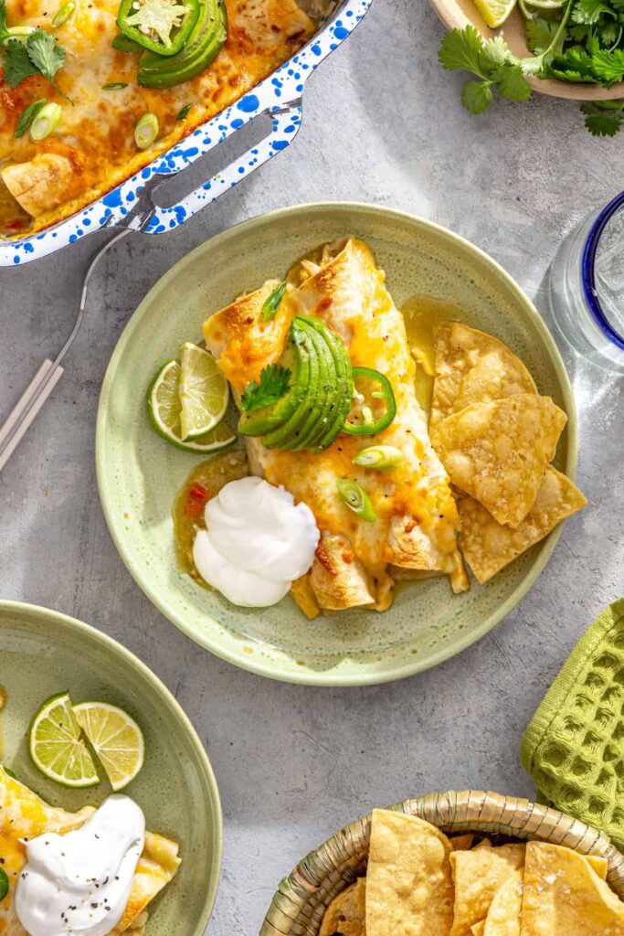 Individual serving of creamy green chicken enchiladas with tortilla chips, sour cream, and lime