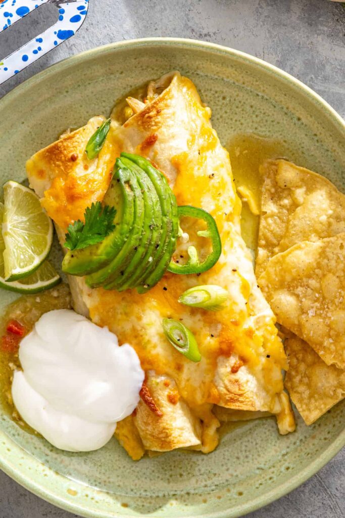 Plated homemade chicken enchiladas topped with avocado and cilantro