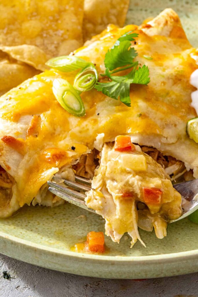 Fork lifting a bite of creamy green chicken enchiladas showing the cheesy shredded chicken filling