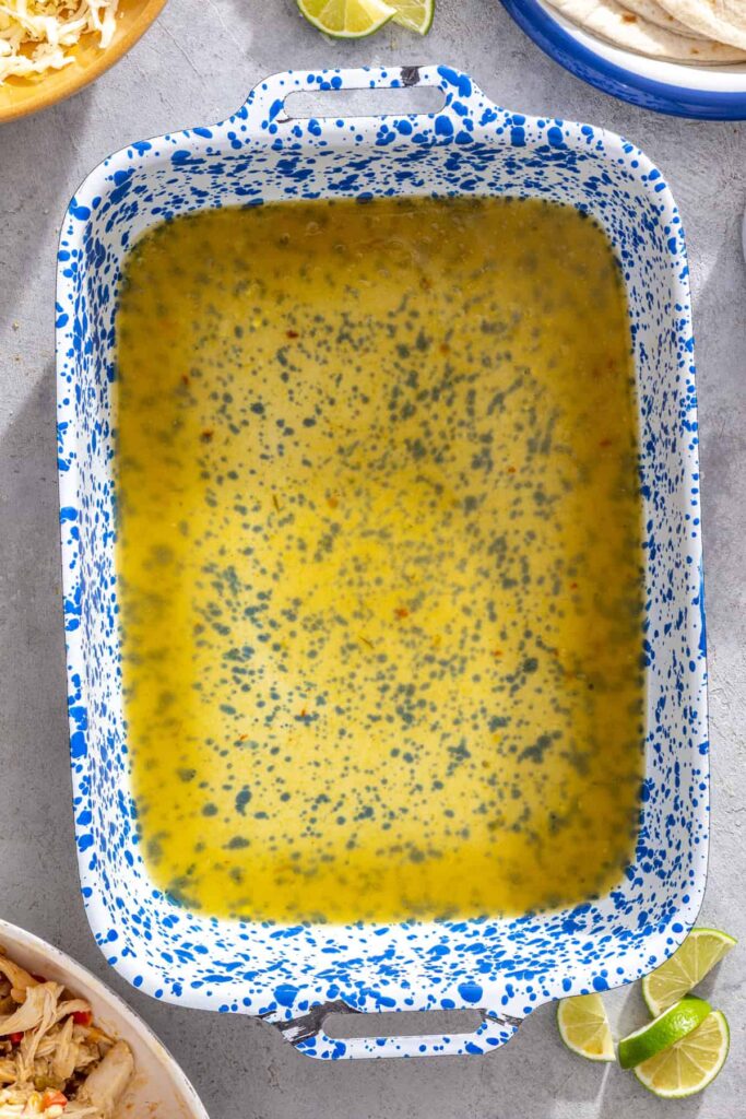 Green enchilada sauce spread across the bottom of a baking dish