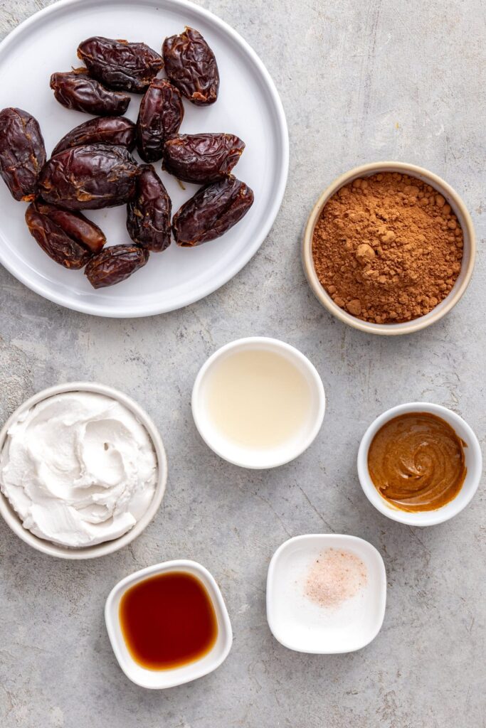 Ingredients for healthy chocolate frosting including Medjool dates, coconut cream, cacao powder, almond butter, and vanilla.