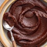 Healthy chocolate frosting made with dates, cacao powder, and coconut cream served in a bowl with a spoon.