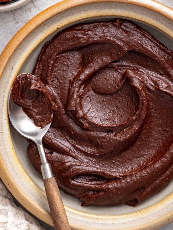 Healthy chocolate frosting made with dates, cacao powder, and coconut cream served in a bowl with a spoon.