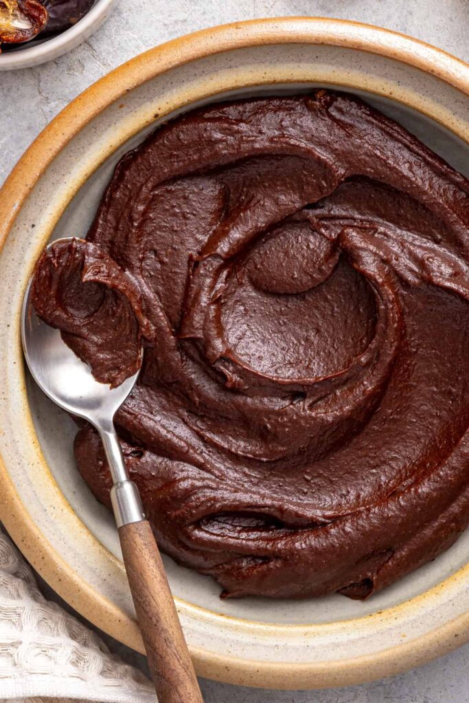 Healthy chocolate frosting made with dates, cacao powder, and coconut cream served in a bowl with a spoon.