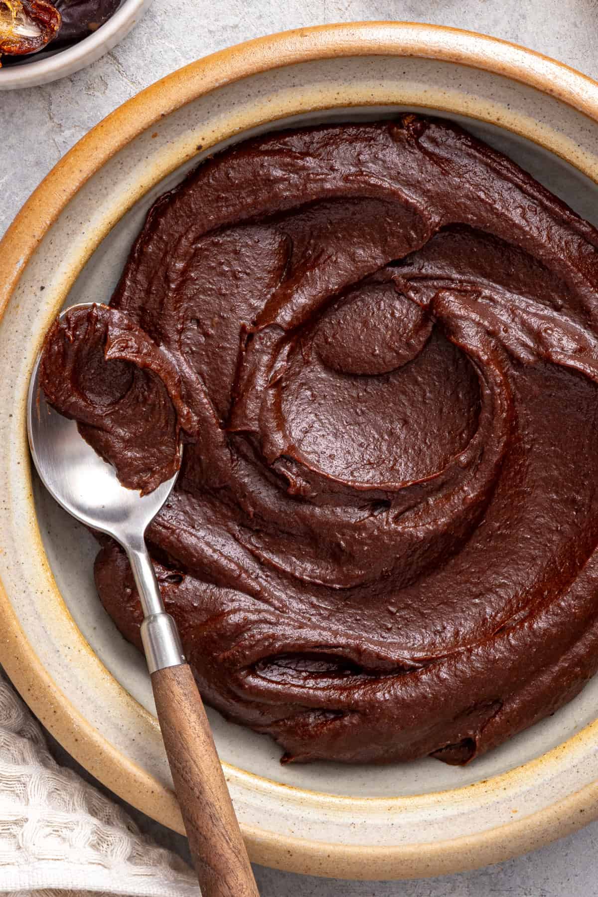 Healthy chocolate frosting made with dates, cacao powder, and coconut cream served in a bowl with a spoon.