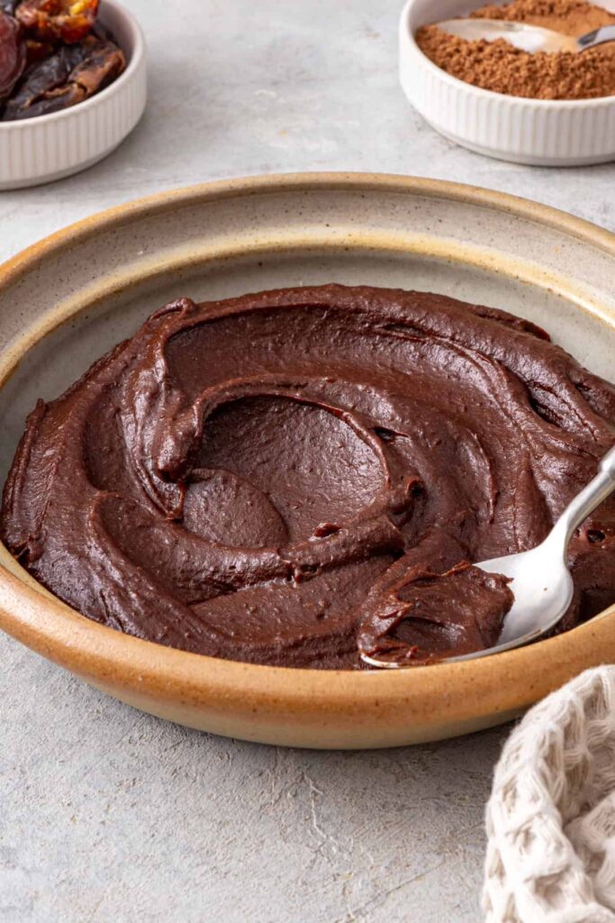 Thick healthy chocolate frosting lifted from the bowl with a spoon