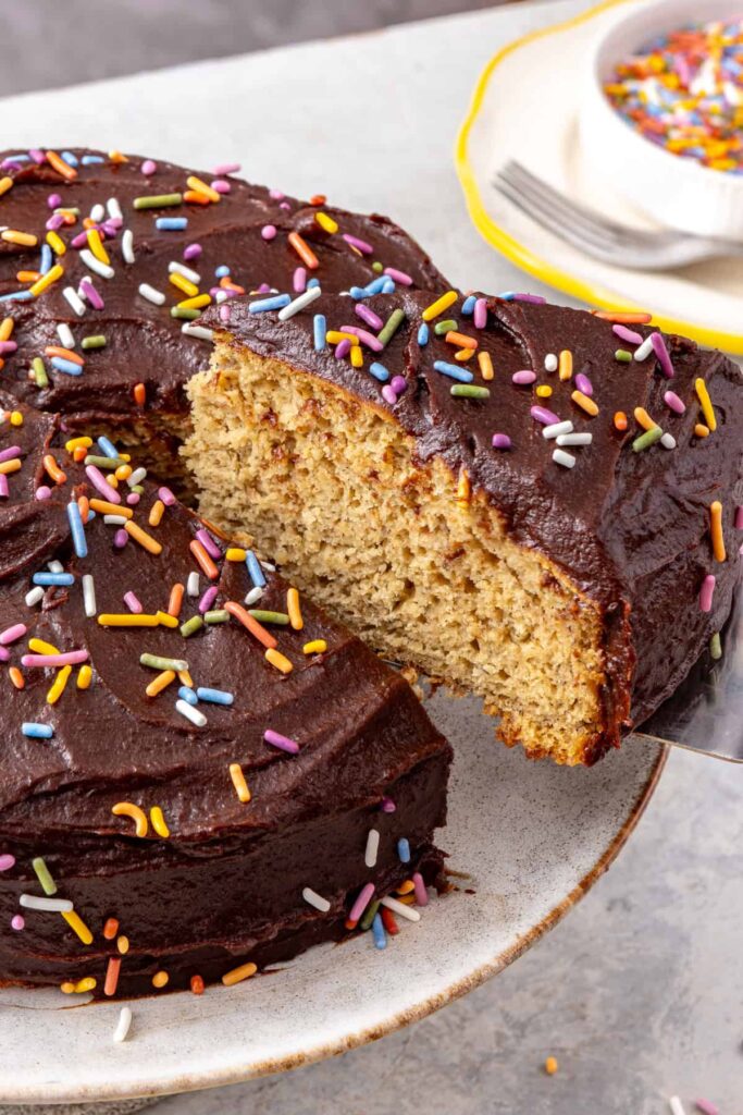 Healthy banana birthday cake with chocolate date frosting and rainbow sprinkles showing soft fluffy texture