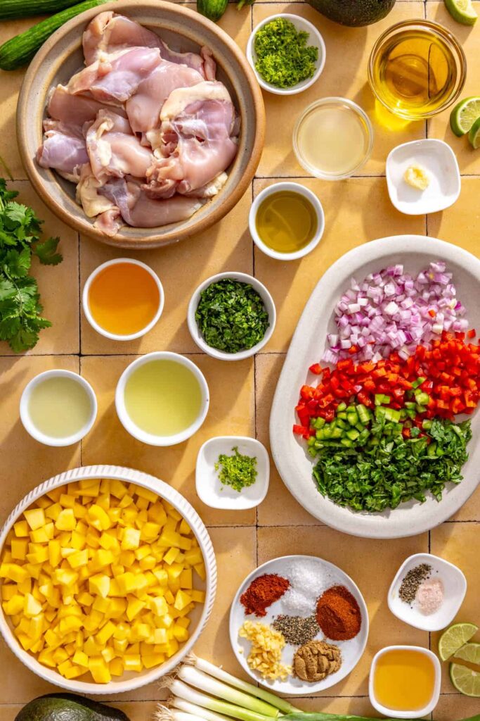 Ingredients for honey lime grilled chicken with mango salsa including chicken thighs, fresh mango, lime, cilantro, garlic, avocado, and spices