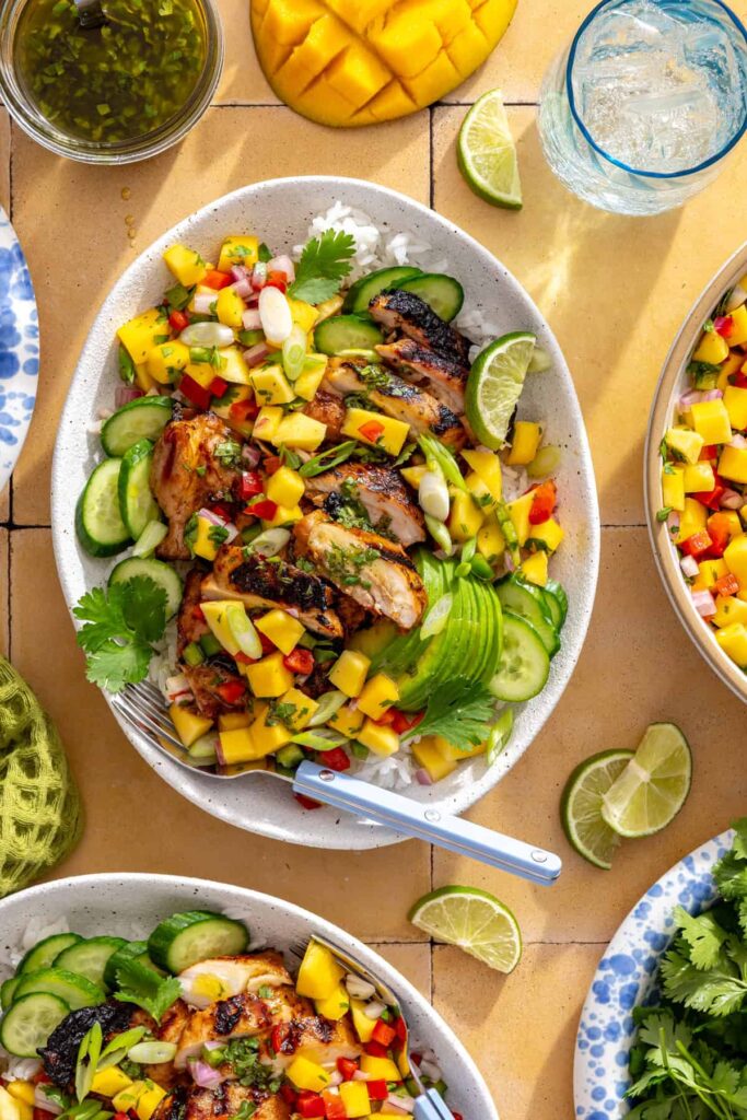 Honey lime grilled chicken served on a platter with mango salsa, cucumber, and lime wedges