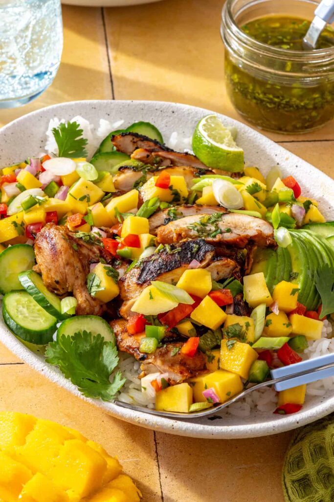 Side view of honey lime grilled chicken with mango salsa, avocado, cilantro, and lime wedges
