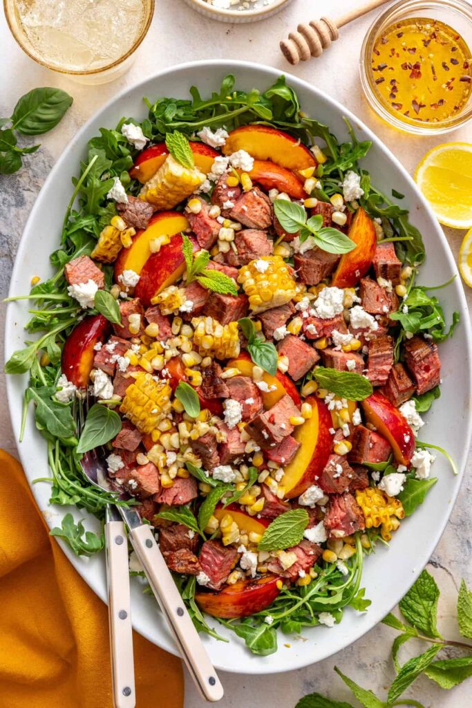 Harissa steak salad with charred peaches, grilled corn, arugula, and feta served in a bowl