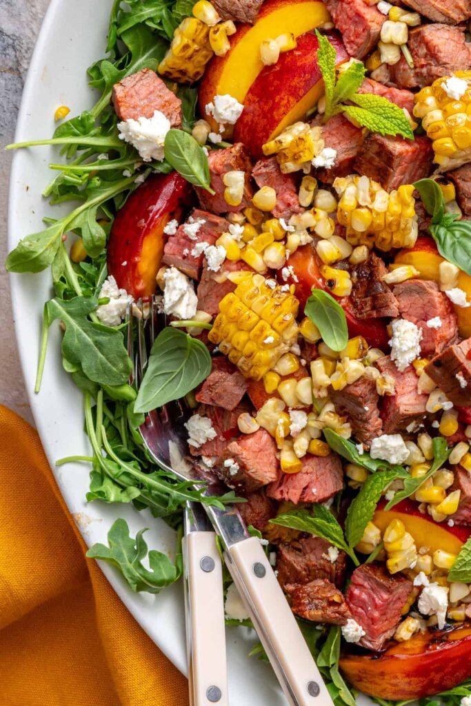 Grilled steak salad topped with fresh herbs, feta, and smoky charred vegetables