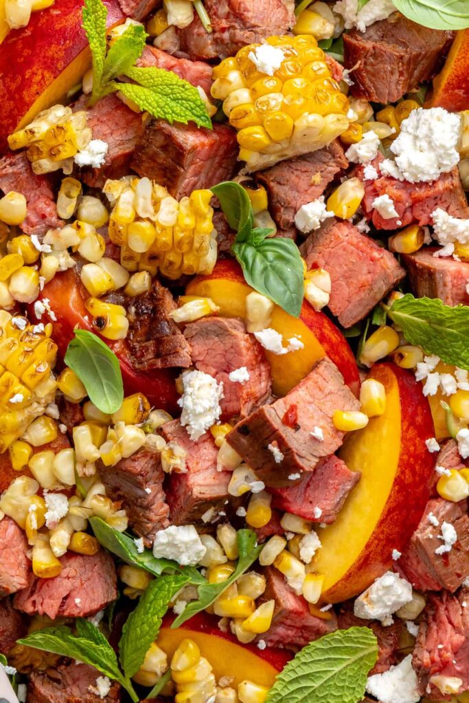 Detailed close-up of colorful steak salad with charred peaches and fresh herbs