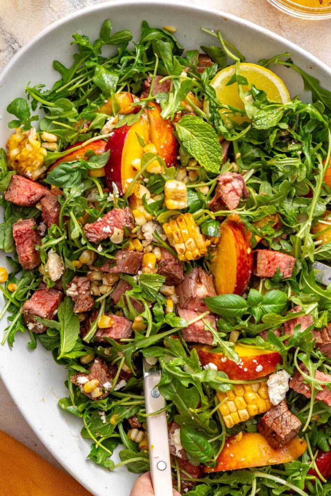 Large bowl of grilled steak salad with serving spoons on a styled table