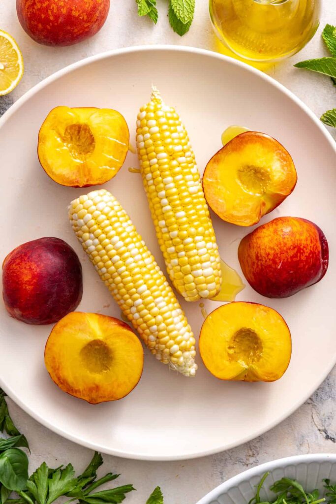 overhead view of sliced peaches and ears of corn, ready to grill for steak salad