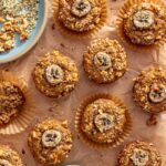 Toddler banana muffins wrapped individually on a styled table with fresh bananas, hemp seeds, and chopped walnuts