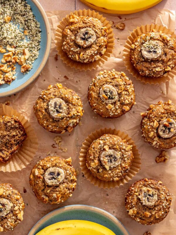 Toddler banana muffins wrapped individually on a styled table with fresh bananas, hemp seeds, and chopped walnuts