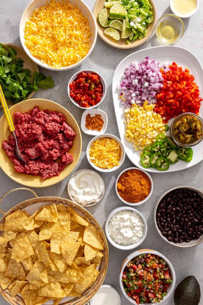 Ingredients for air fryer nachos with ground beef, black beans, tortilla chips, cheese, vegetables, and cottage cheese queso