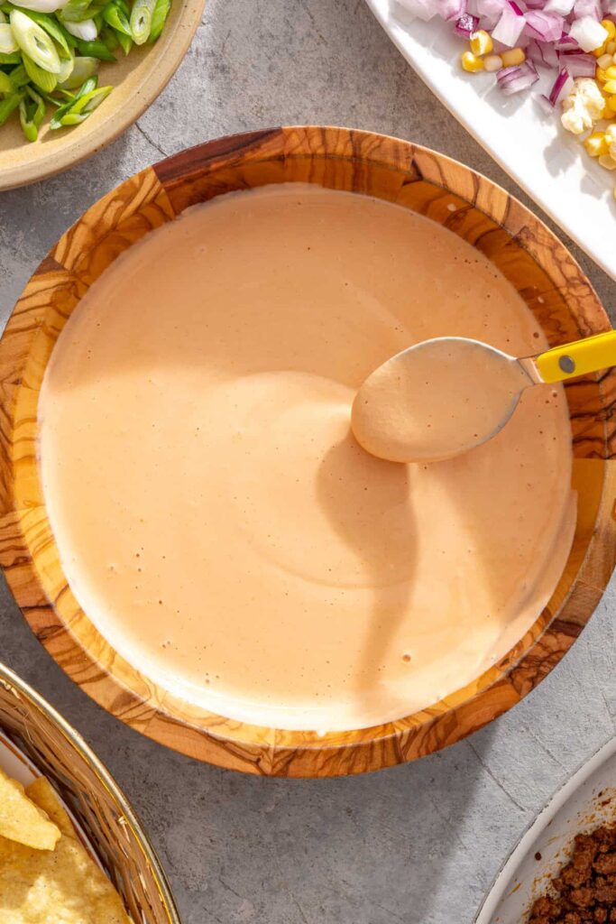 spoon stirring a high-protein cottage cheese queso dip for nachos