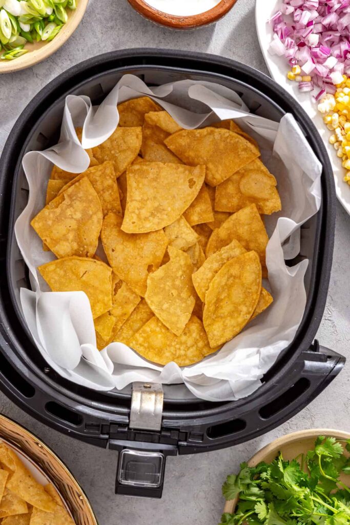 First layer of tortilla chips in a parchment-lined air fryer basket
